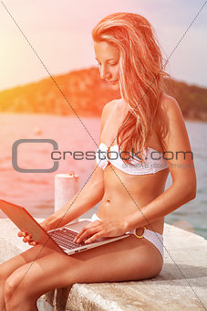 Woman sitting and relaxing on a beach with a laptop