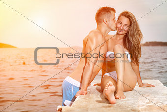 Young happy couple kiss on a beach during sunset
