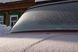 The car covered with frost, against the old wooden house.