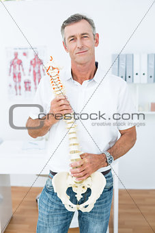 Doctor looking at camera and showing anatomical spine