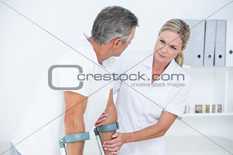 Doctor helping her patient walking with crutch