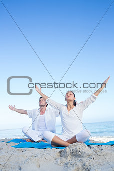 Happy couple doing yoga beside the water