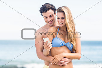 Happy couple in swimsuit looking at mobile phone