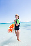 Fit blonde woman standing in the water and holding surfboard