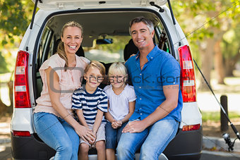 Happy family of four sitting in car trunk