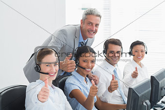 Colleagues with headsets using computers while gesturing thumbs up