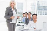 Smiling businesswoman looking at camera while work team using computer