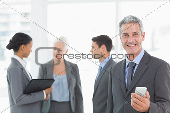 Businessman using a smartphone with colleagues behind in office