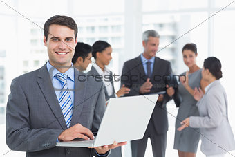 Businessman using laptop with colleagues behind