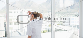 Wear view of confident female doctor looking through windows