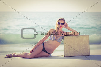 Stylish blonde leaning on suitcase on the beach