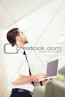 Composite image of sophisticated businessman standing using a laptop