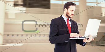 Composite image of focused businessman using his laptop