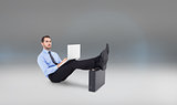 Composite image of businessman sitting on the floor with feet up on suitcase