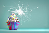 Delicious cupcake with a glittering sparkler and smarties on a whipped cream. Colored disks background.