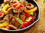 Beef Fajitas with colorful bell peppers in pan on a wooden table