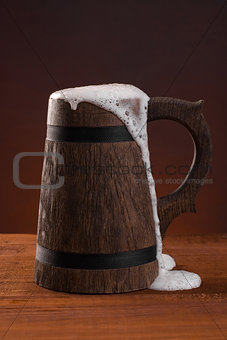 Wooden beer mug with foam on a dark red background.