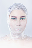 Misterous pretty woman wrapped in cellophane looking forward standing on light grey background