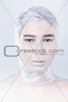 Misterous pretty woman wrapped in cellophane looking forward standing on light grey background