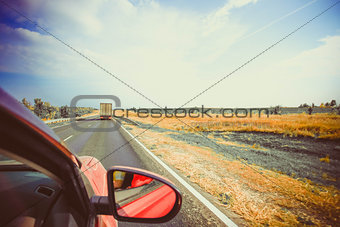Rear view mirror and long road through arid landscape