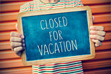 young man with a chalkboard with the text closed for vacation