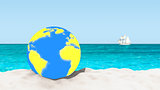 Ball with a world map pattern on a sandy beach with a blurred background.