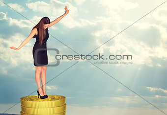 Businesswoman standing on coins stack in balance