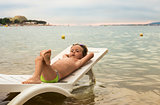 Serious little boy resting on lounger by sea at sunset