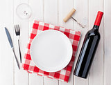 Table setting with empty plate, wine glass and red wine bottle