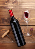 Red wine bottle, glass and corkscrew on wooden table
