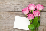 Pink roses bouquet and blank greeting card over wooden table