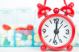 Medicine in weekly pill box and red alarm clock