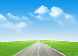 Asphalt road through the green field and blue sky