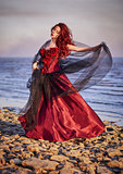 Beautiful young woman in red dress standing on sea coast