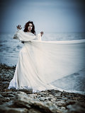 Beautiful sad young woman in white dress standing on sea coast