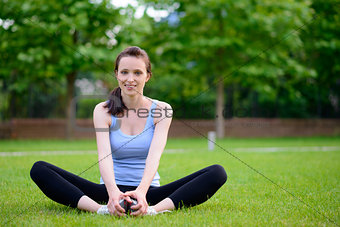 Beautiful Smiling Woman Doing Stretching Exercise on the Grass in the Park