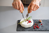 Woman's hands using cheese knife and fork to cut Camembert
