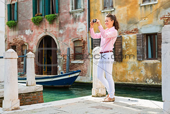 Happy woman tourist in Venice taking photos near canal