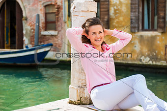 Laughing woman sitting against pillar on pier in Venice