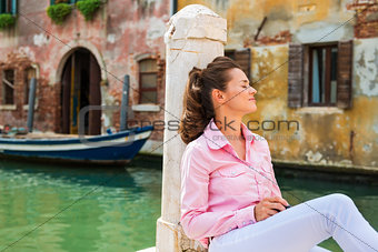 Woman sitting and relaxing on pier in Venice with eyes closed