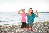 Young mother and daughter in fitness gear on beach flexing arms
