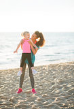 Fit young mother lifting young daughter up on beach at sunset