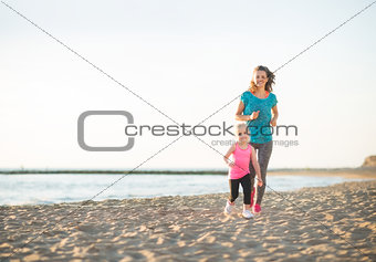 Happy mother and daughter running on beach at sunset