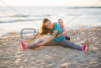 Happy mother exercising with daughter on the beach at sunset