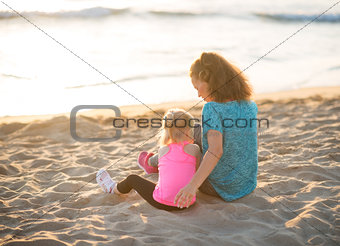 Young mother and daughter in workout gear sitting on beach