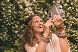 happy bohemian young woman among flowers playing with retro came