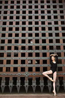 Slim dancer stands on one leg near the old gate