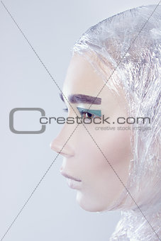 Profile of misterous pretty woman wrapped in cellophane looking forward standing on light grey background