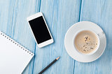 Coffee cup, smartphone and blank notepad on wooden table backgro