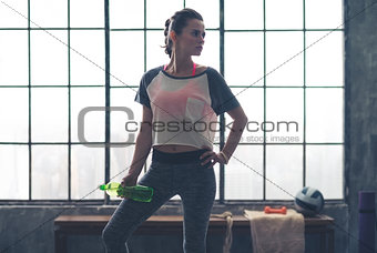 Fit woman in workout gear looking over shoulder holding water